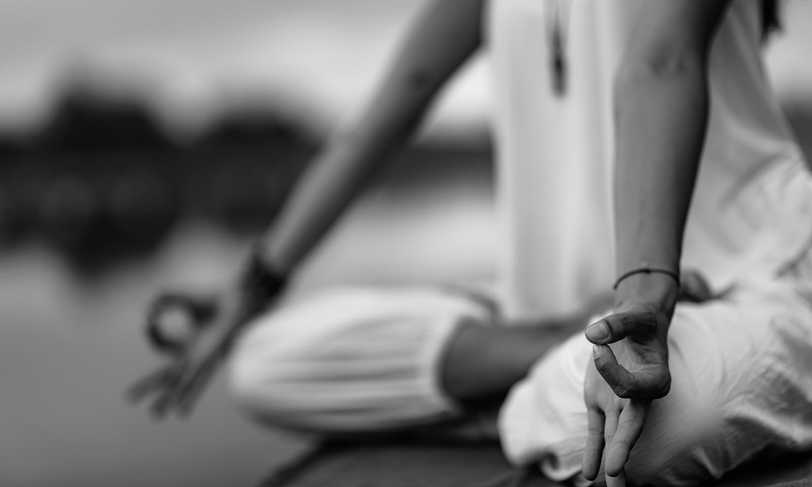 Woman doing yoga by the lake, sitting in lotus pose with fingers in mudra position.